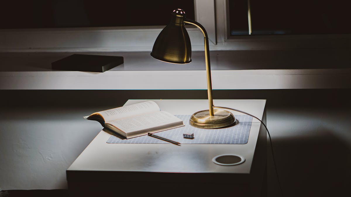 A warm reading lamp illuminating an open book on a wooden desk